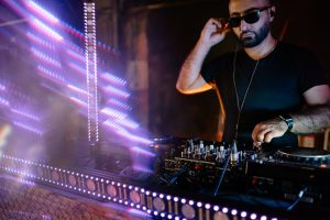 A DJ performs at a lively nightclub with colorful lights and music equipment.