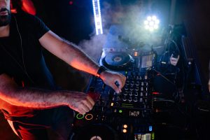 DJ skillfully mixes tracks with vibrant lighting and audio equipment in a dynamic nightlife setting.